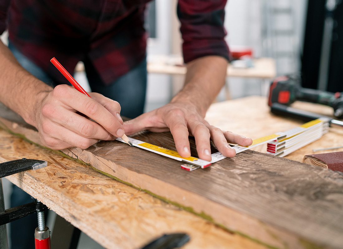 Insurance by Industry - Closeup View of a Male Carpenter Carefully Measuring a Piece of Wood in his Workshop