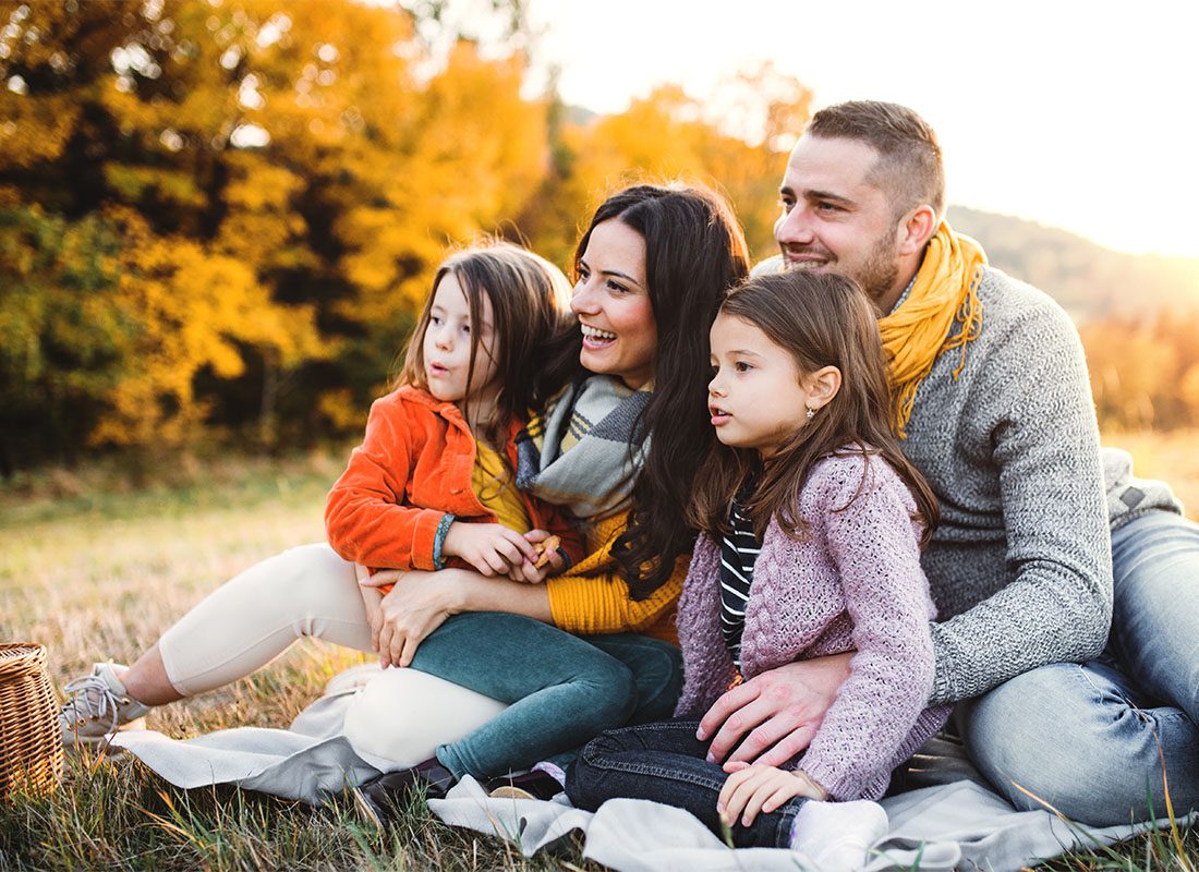 Personal Insurance - Portrait of Cheerful Parents Having Fun Sitting with Their Two Daughters on the Grass in the Park During the Fall Season