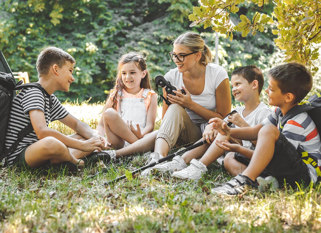 Ministry Insurance - View of a Cheerful Young Female Teacher Teaching a Small Group of Kids About the Outdoors During a Summer Camping Trip