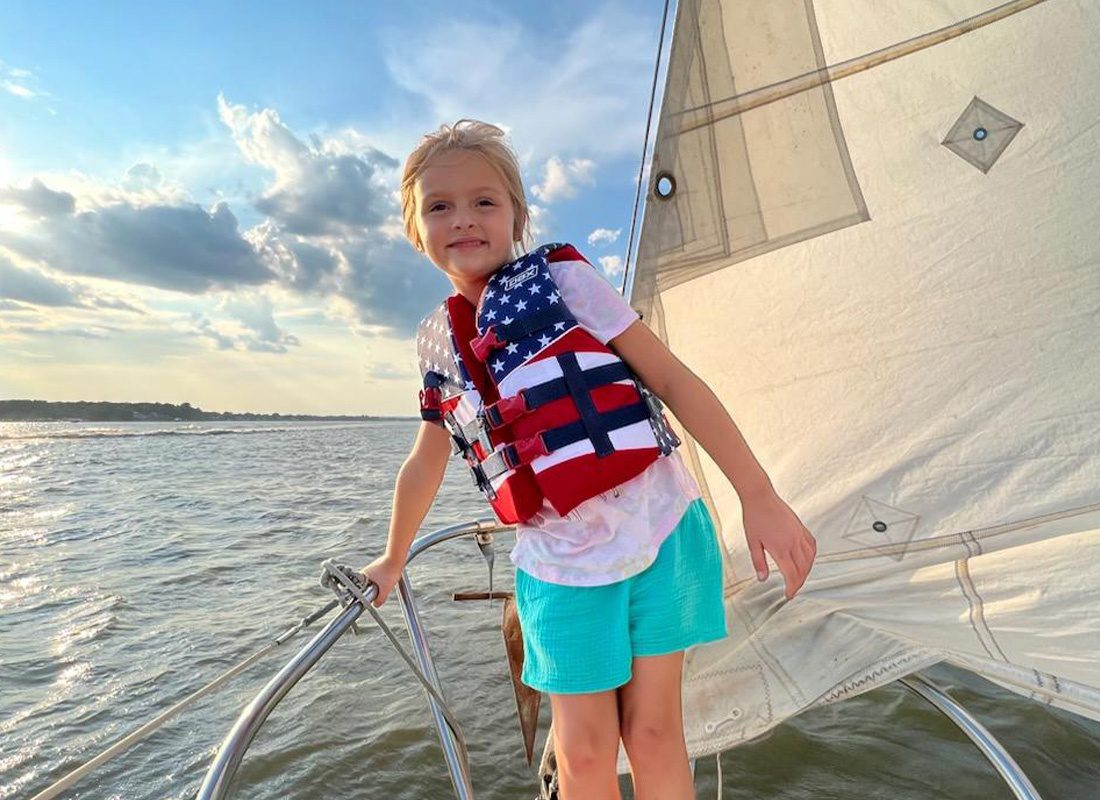 Child Life Insurance - Smiling Child with Life Vest Standing on a Sail Boat at Dusk