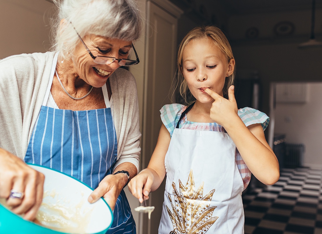 Life Insurance and Annuities - Portrait of a Cheerful Grandmother Having Fun Making a Cake with her Granddaughter in the Kitchen