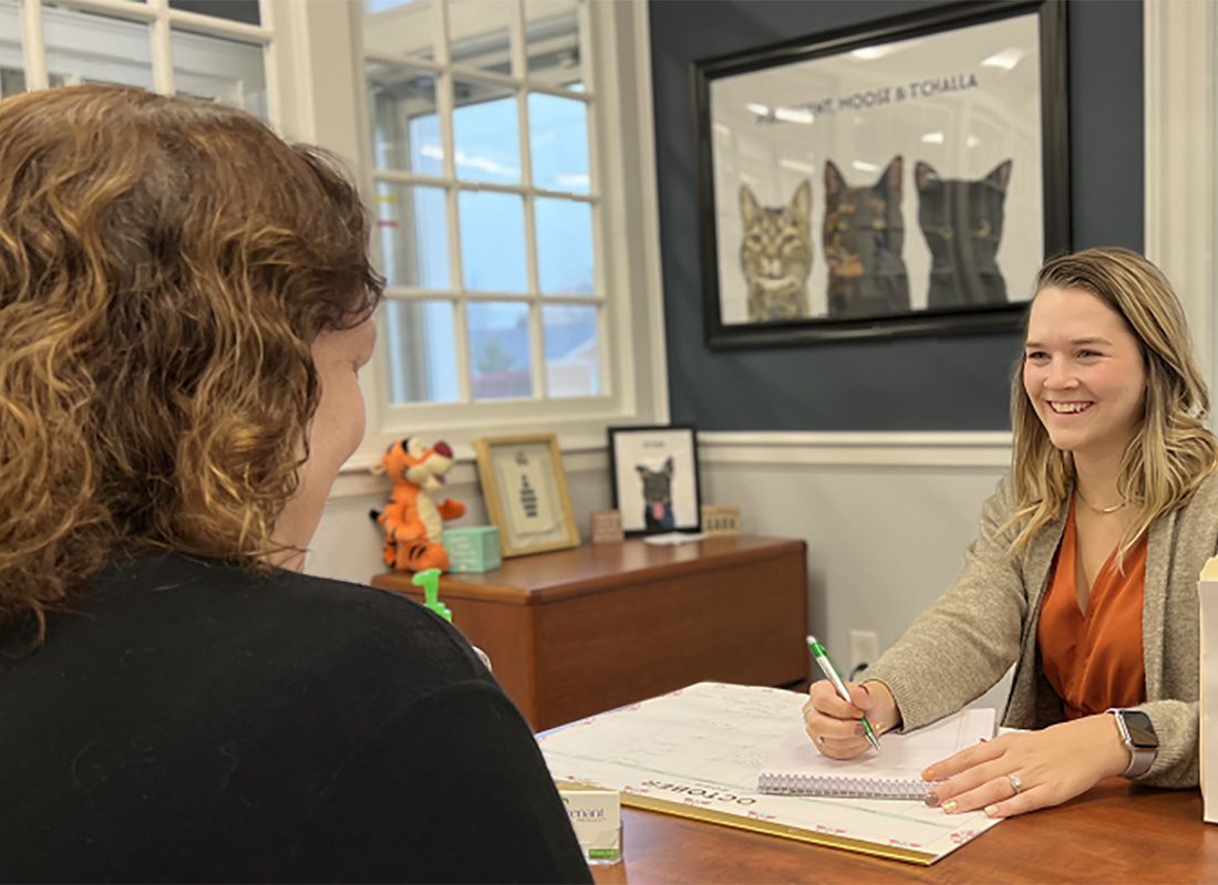 Policy Review - Portrait of a Smiling Female Covenant Insurance Employee Sitting Behind her Desk During a Meeting with a Woman to Review her Insurance Policy